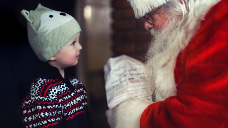Santa holding list in front of small boy in Christmas sweater and knit cap